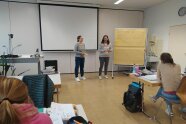 2 Personen stehen neben einer Pinnwand in einem Klassenzimmer