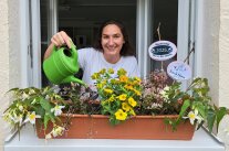 Frau gießt Blumenkasten auf dem Fensterbrett