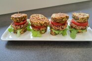 Vier kleine Burger auf einem rechteckigen Teller angerichtet.