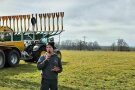Mann mit einem Mikrofon steht vor einer großen Maschine mit Anbau zur Gülleausbringung